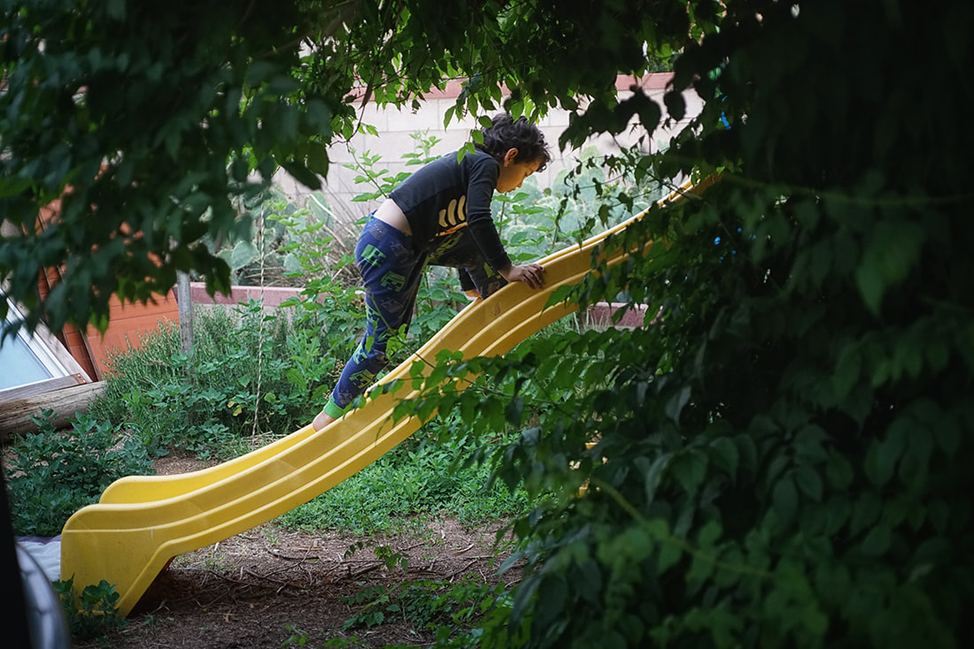 boy climbs up slide under vines